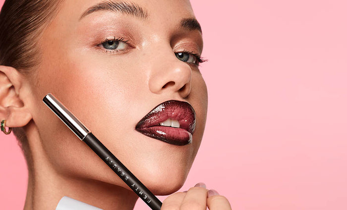 Model wearing Trace'd Out Pencil Lip Liner and holding Trace'd Out Lip Pencil Liner in Coal Blooded. Model wearing Trace'd Out Pencil Lip Liner and holding Trace'd Out Lip Pencil Liner in Coal Blooded.