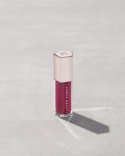 A closed tube of Gloss Bomb Universal Lip Luminizer in the shade Fuschia Flex on a grey background. A closed tube of Gloss Bomb Universal Lip Luminizer in the shade Fuschia Flex on a grey background.