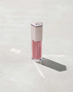 A closed tube of Gloss Bomb Universal Lip Luminizer in the shade Fu$$y on a grey background.