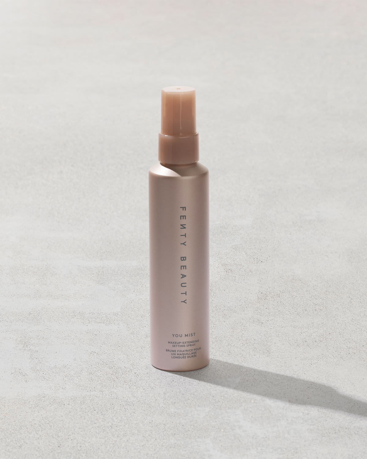 You Mist Makeup-Extending Setting Spray bottle on a concrete backdrop.