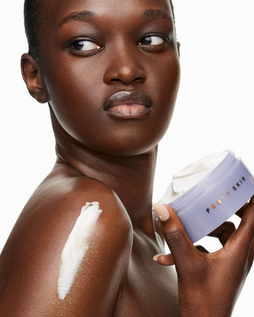 Model holding open tub of Butta Drop Whipped Oil Body Cream with Tropical Oils + Shea Butter with product applied to shouler.