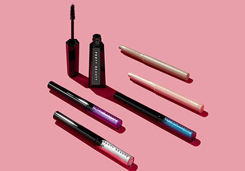 Open shot of Hella Thicc Mascara tube standing up with Glitty Lid Eyeliner and Shadowstix horizontal against a pink background.